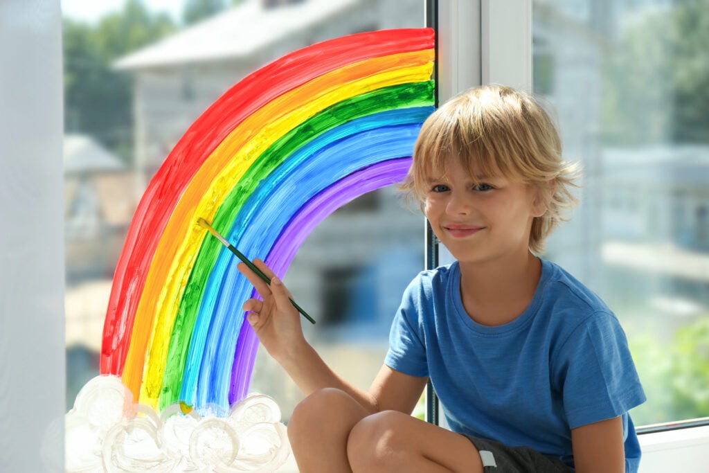 A child is painting a rainbow on a window