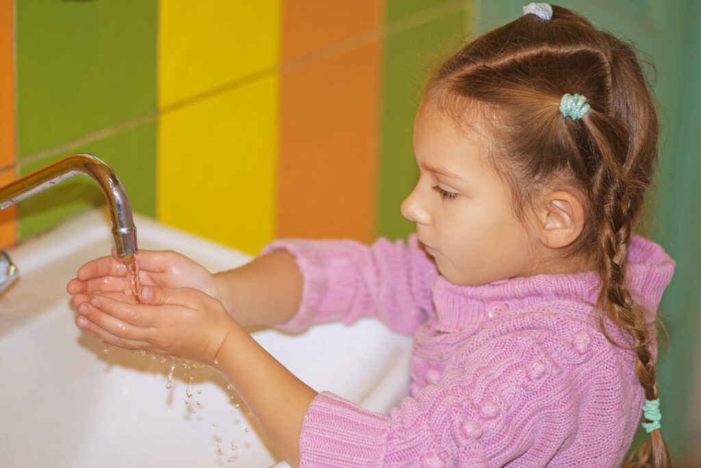 little girl in pink sweater washes hands