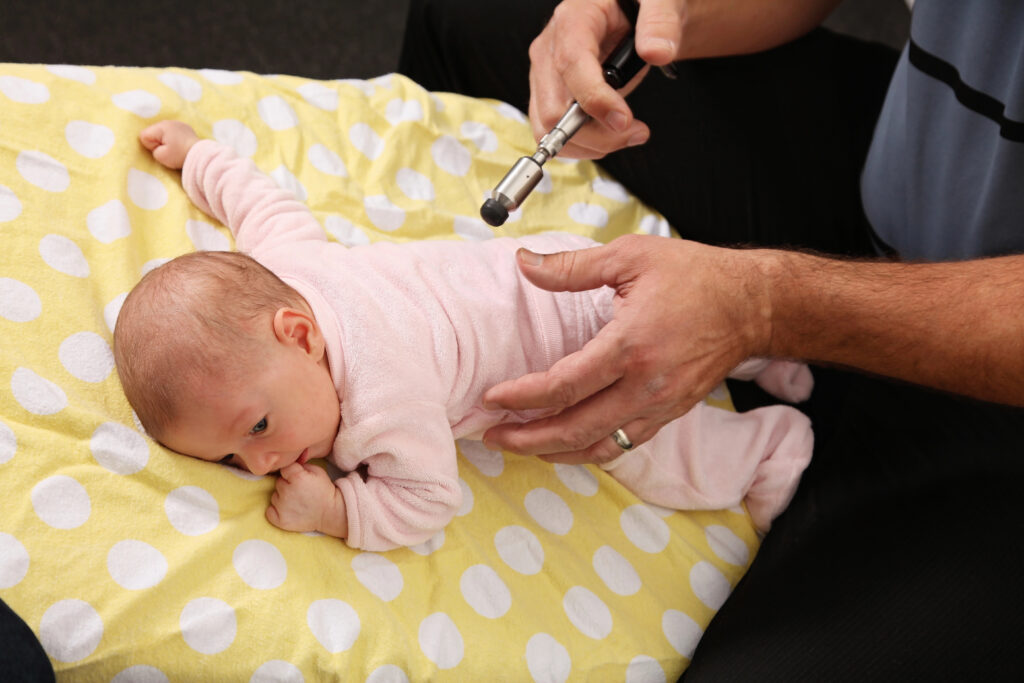 Chiropractor uses an activator on an infant