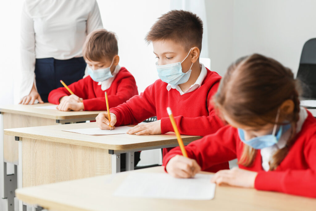 Pupils in medical masks passing exam at school. Concept of epidemic