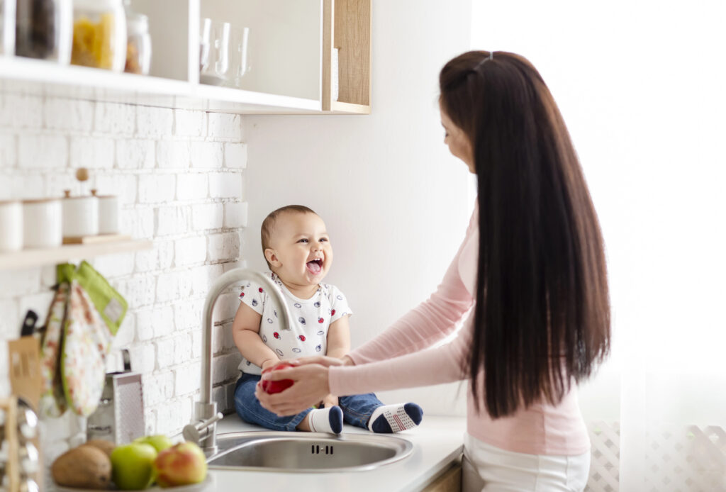 Woman washes apple while caring for baby