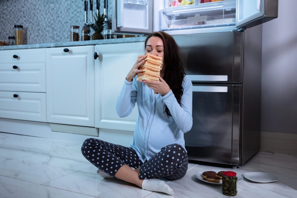 Woman sits on floor eating bread at night