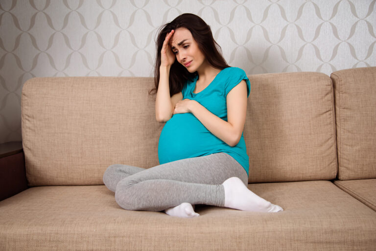 Depression in pregnant women. A young pregnant woman is crying while sitting on the sofa at home.