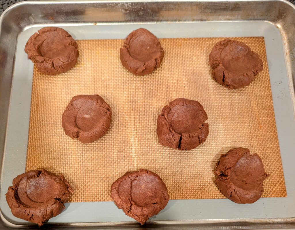 unbaked chocolate thumbprint cookies on a baking sheet