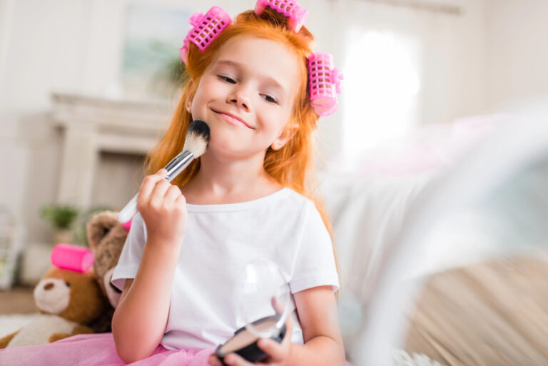 Little girl applies makeup to her face using brush while wearing curlers