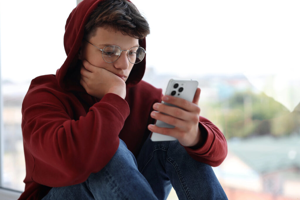 A teen boy in a hoodie is depressed as he looks at his phone