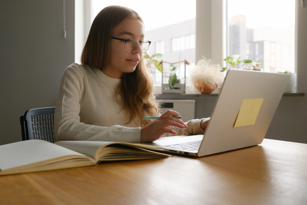 Young girl focused on studying with a laptop, surrounded by books and notebooks